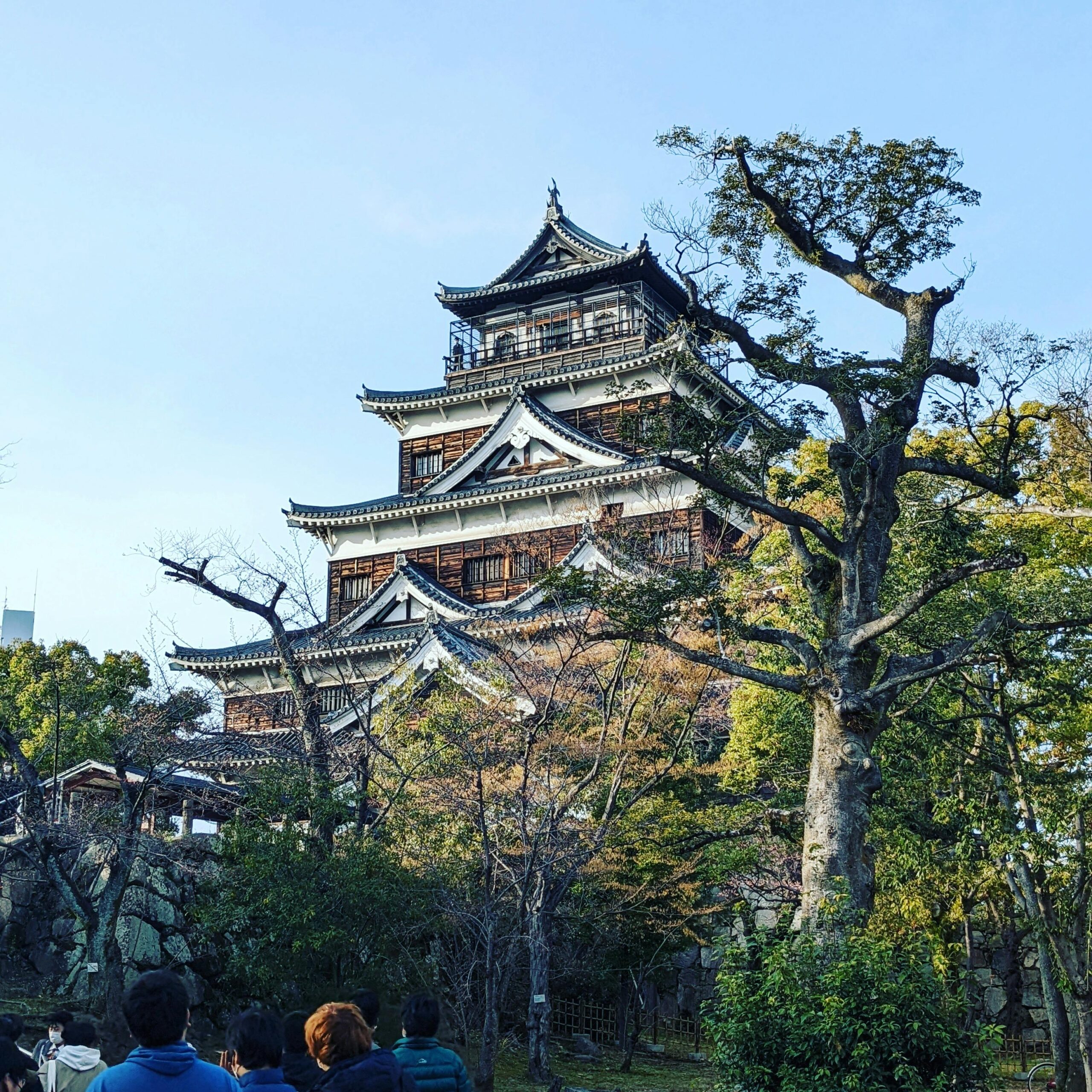 Capturing the grand architecture of Hiroshima Castle amidst lush trees under a clear sky.
