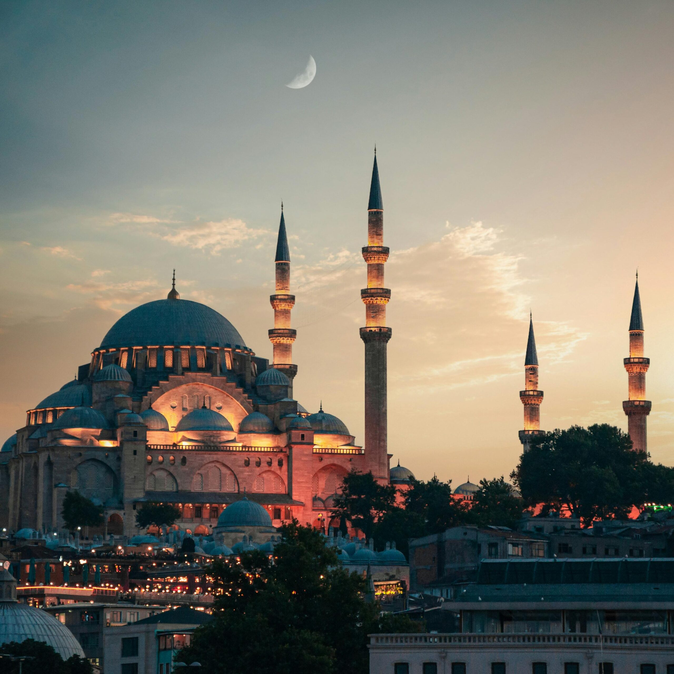 Suleymaniye Mosque illuminated in Istanbul at dusk, showcasing its Ottoman architecture under a crescent moon.